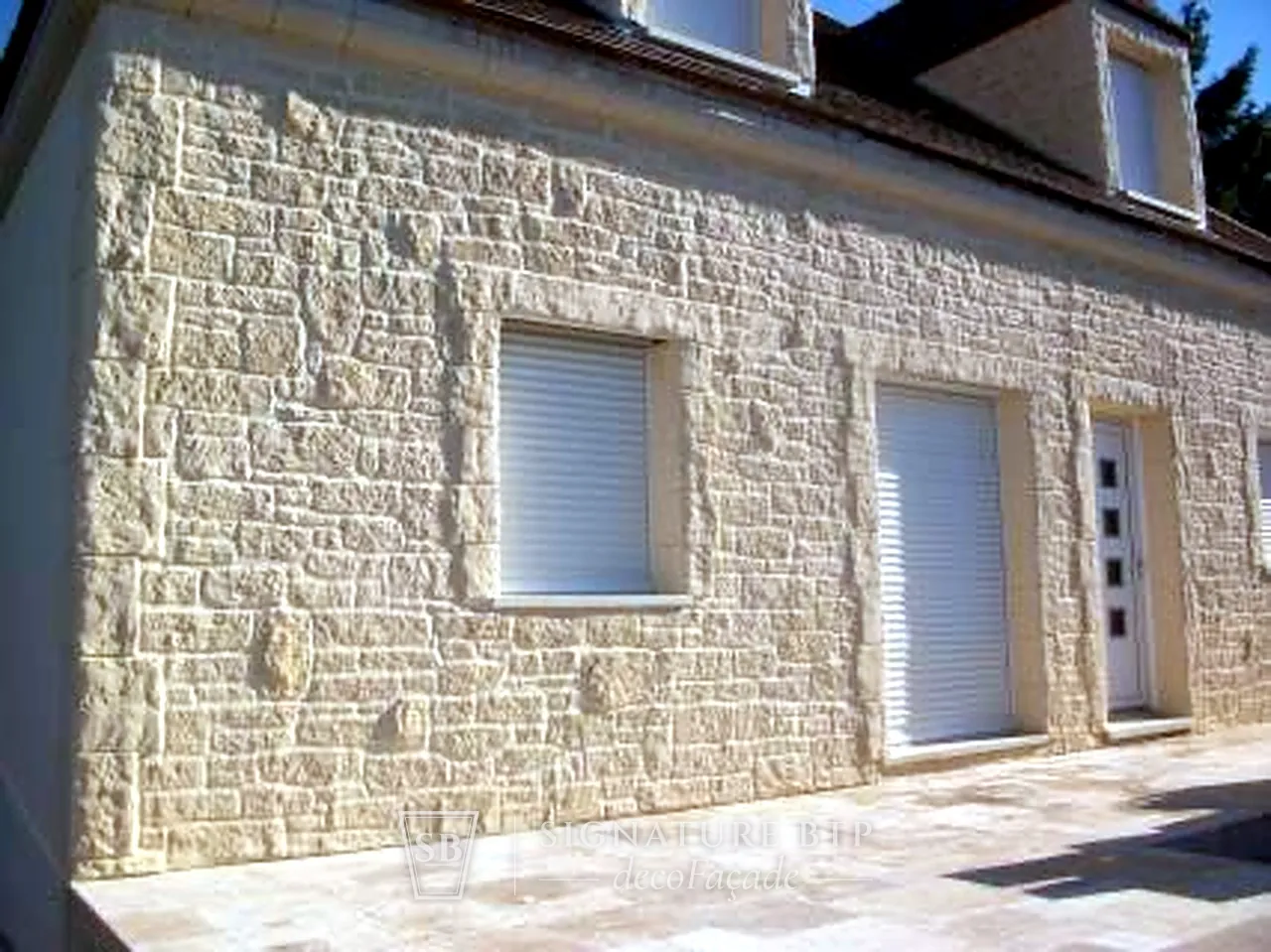 Façade de maison en pierre de taille rustique avec encadrements en relief autour des ouvertures