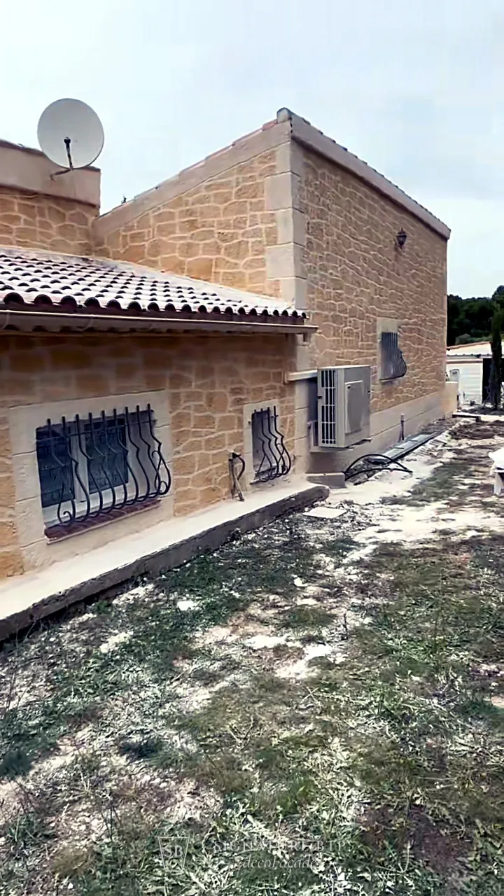 Façade de maison en pierres dorées sculptées avec fenêtres à grilles en fer forgé