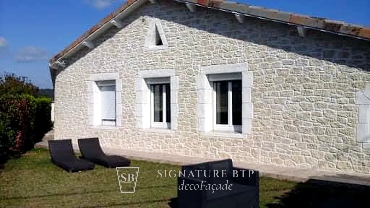 Longère en pierres blanches sculptées avec encadrements de fenêtres, pelouse et transats au premier plan
