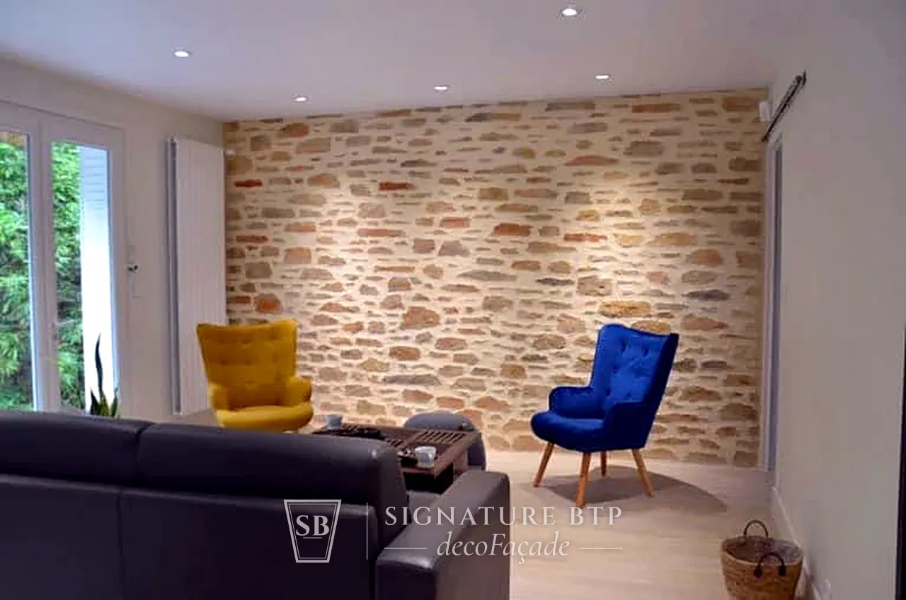 Mur de salon en pierres sculptées aux teintes ocre et grises, fauteuils jaune et bleu devant
